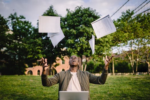 Happy young black male freelancer throwing papers while celebrating successful project during remote work in green park